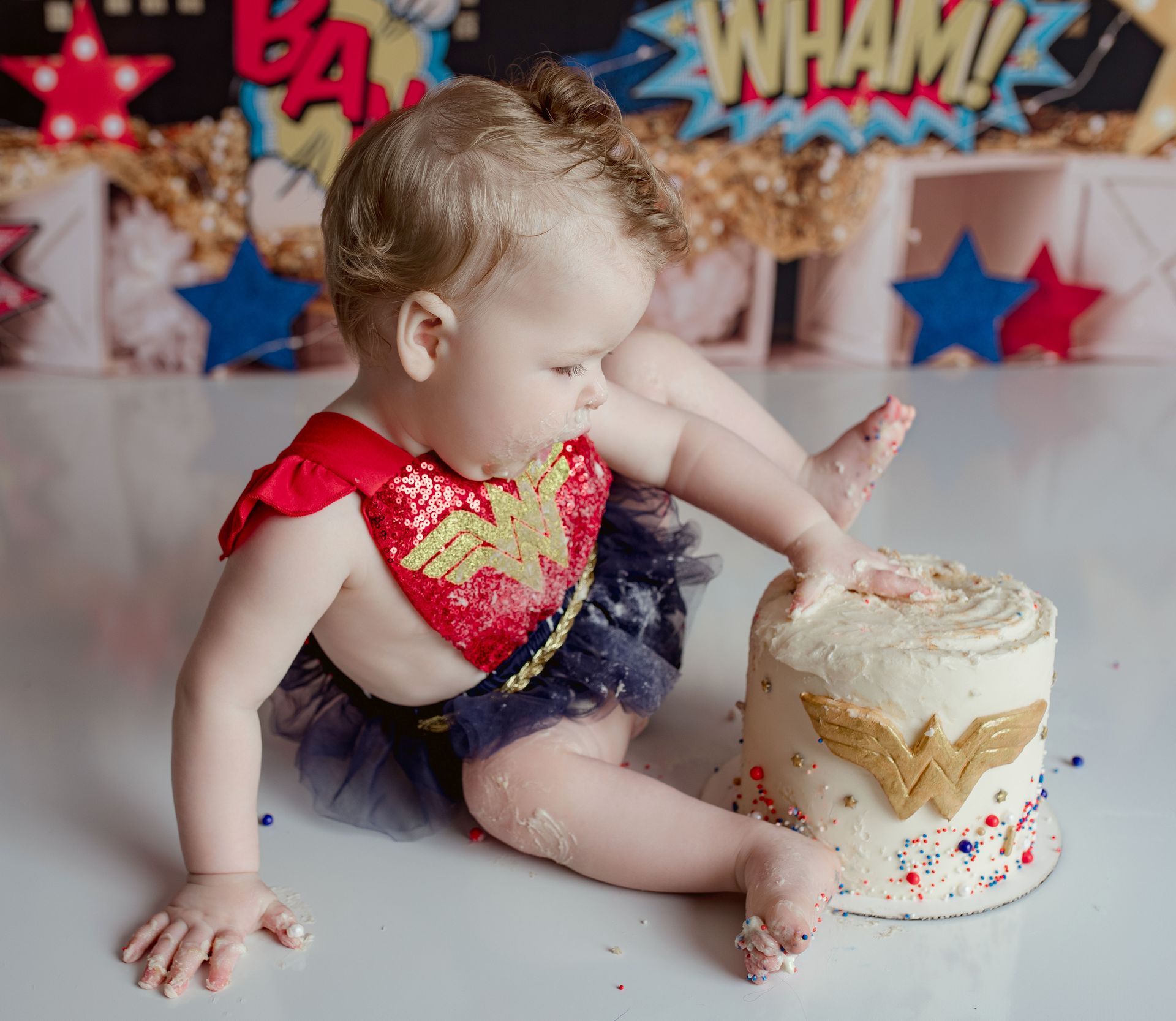A baby in a wonder woman outfit is eating a cake.