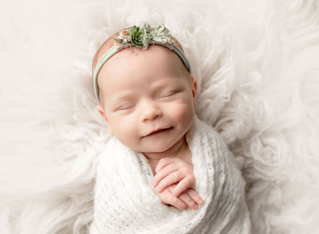 A newborn baby is wrapped in a white blanket and wearing a headband.