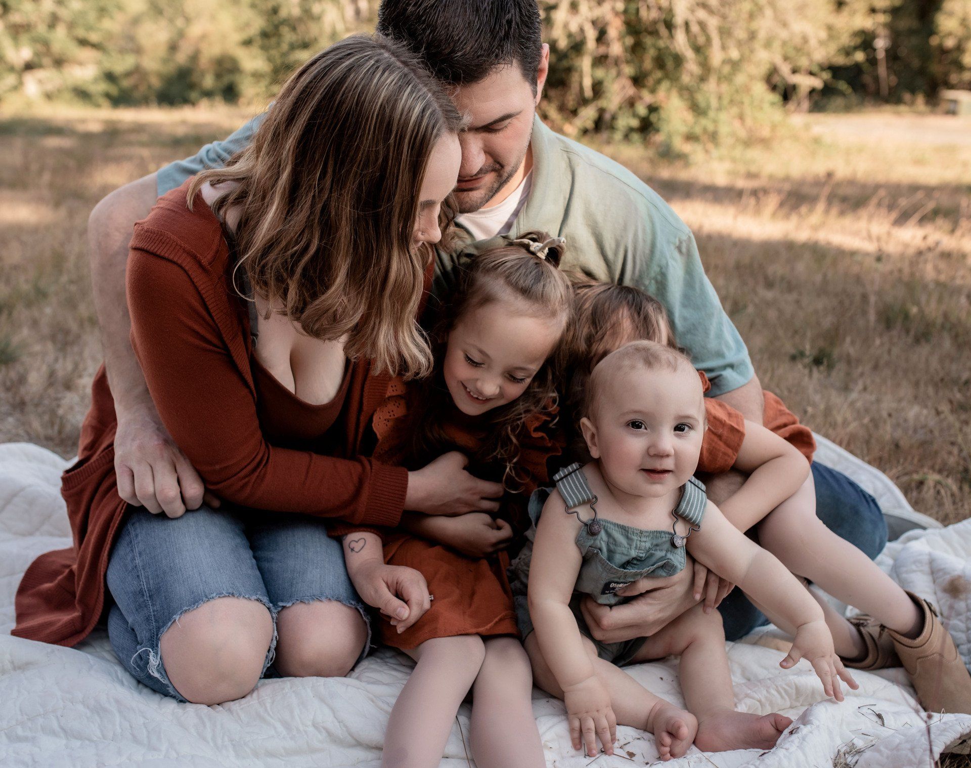 A family is sitting on a blanket in a field.