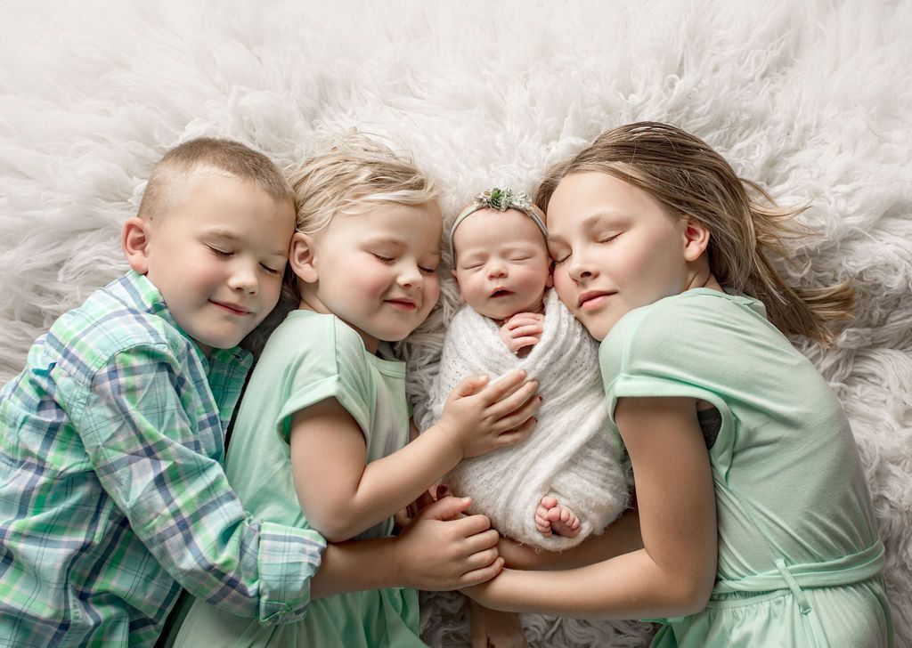 A group of children are laying on a bed holding a newborn baby.