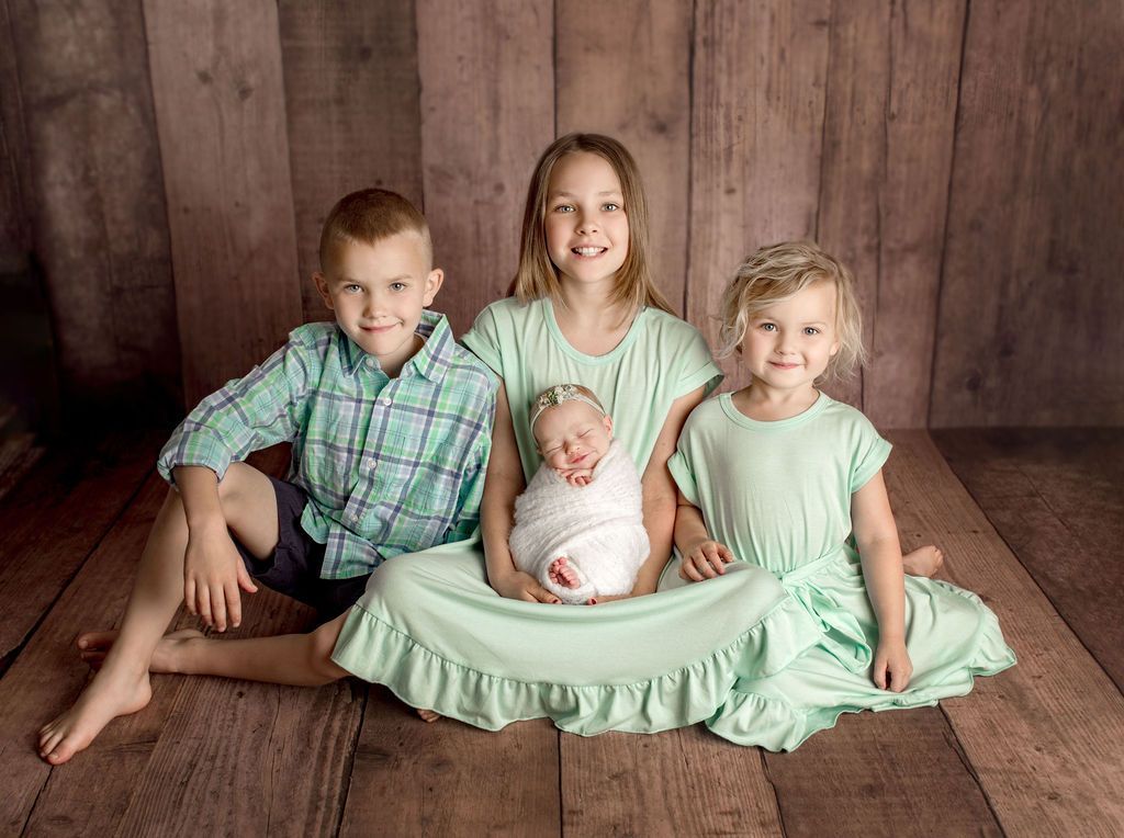 A group of children are sitting on a wooden floor holding a newborn baby.