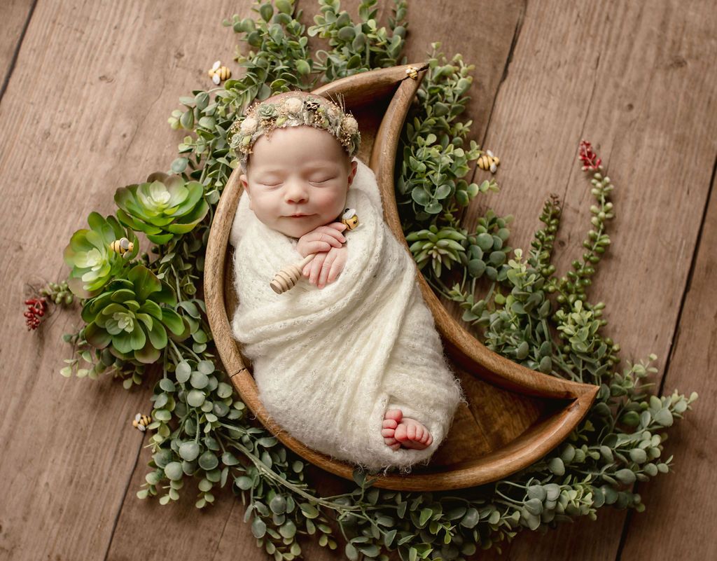 A newborn baby wrapped in a white blanket is sleeping in a wooden crescent moon.