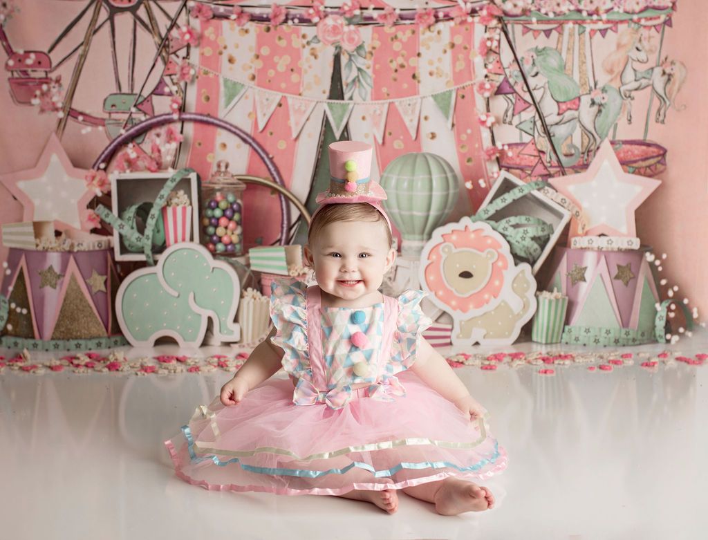 A little girl in a pink dress and crown is sitting on the floor.