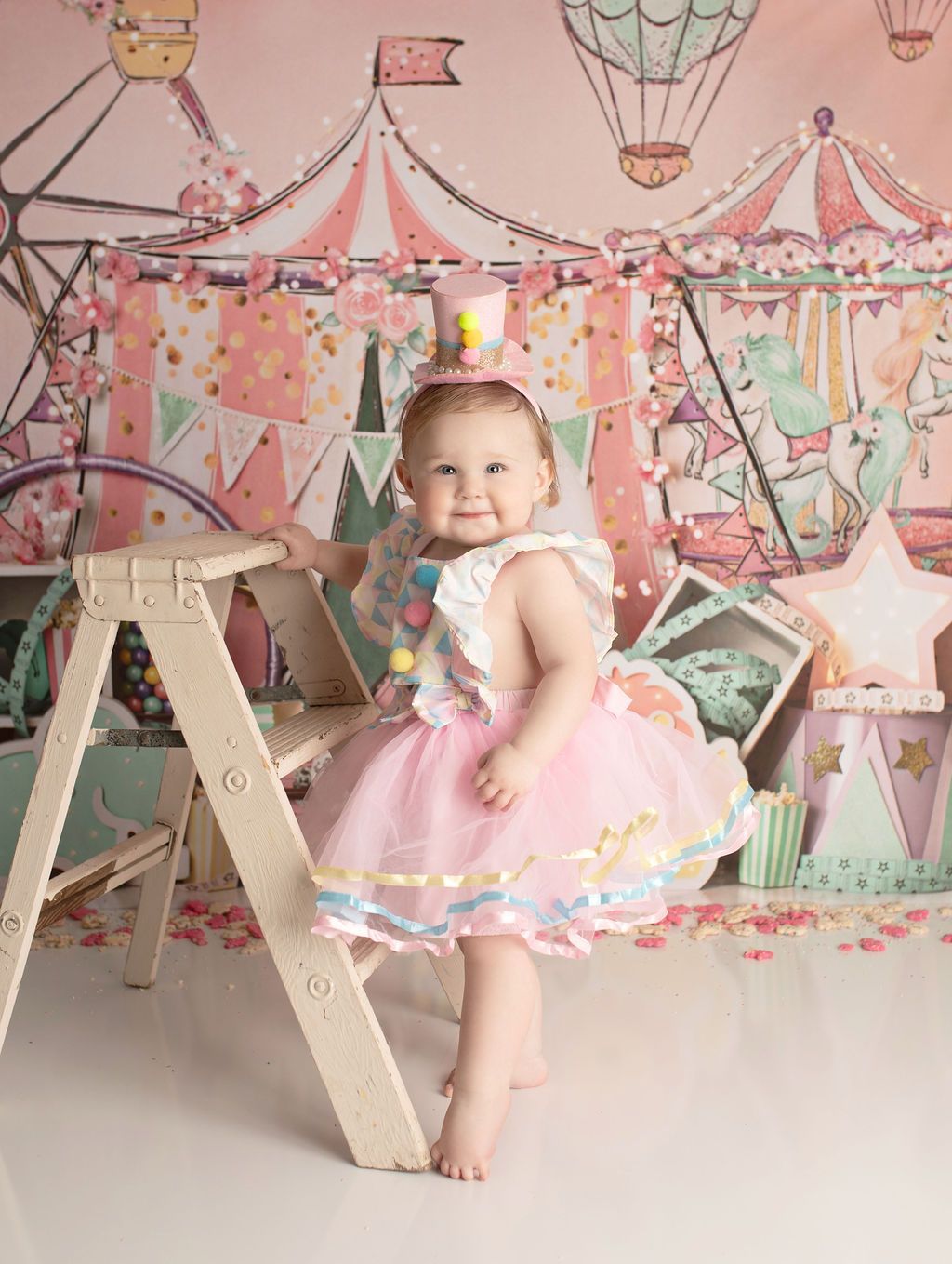 A little girl in a pink dress and top hat is standing next to a ladder.