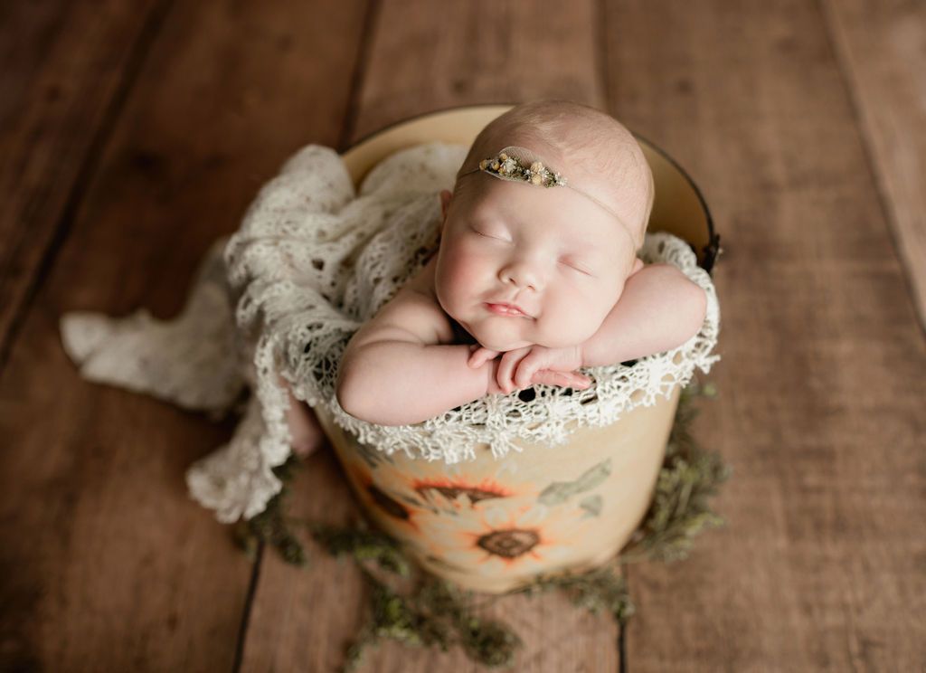 A newborn baby is sleeping in a bucket on a wooden floor.