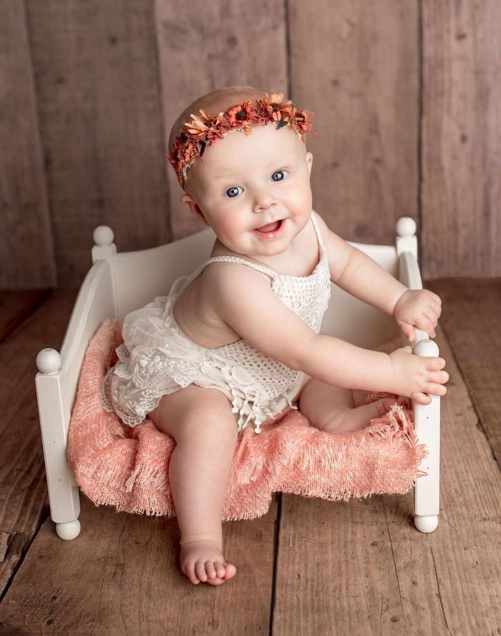 A baby is sitting on a bed with a flower crown on her head.
