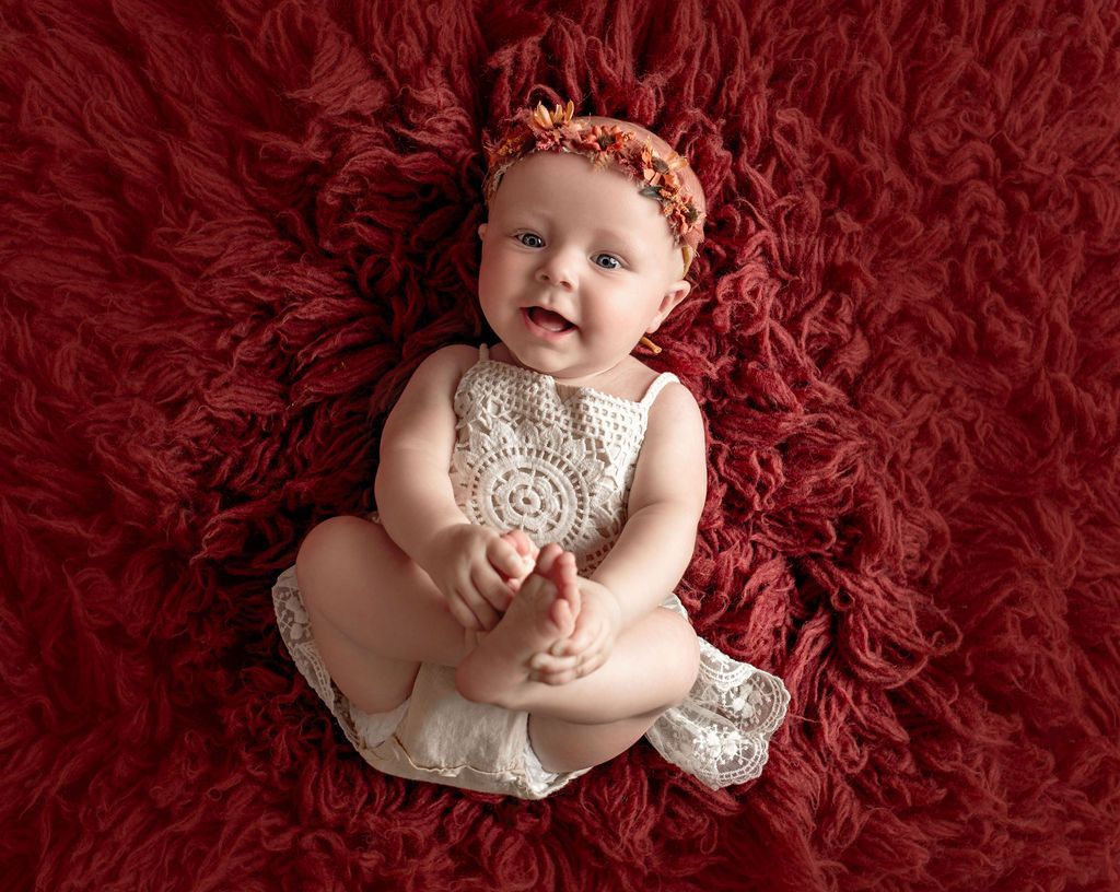 A baby in a diaper is sitting on a red blanket.