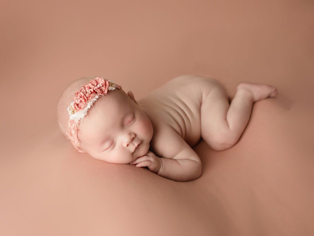 A newborn baby girl wearing a pink headband is sleeping on a pink blanket.