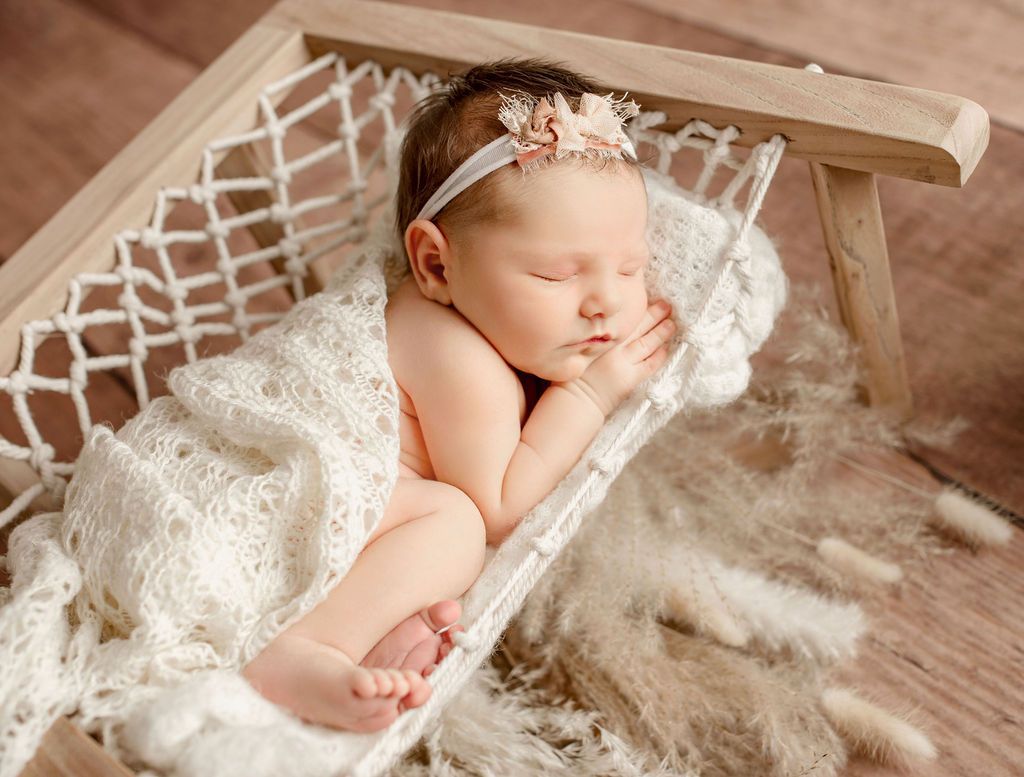 A newborn baby girl is sleeping in a hammock.