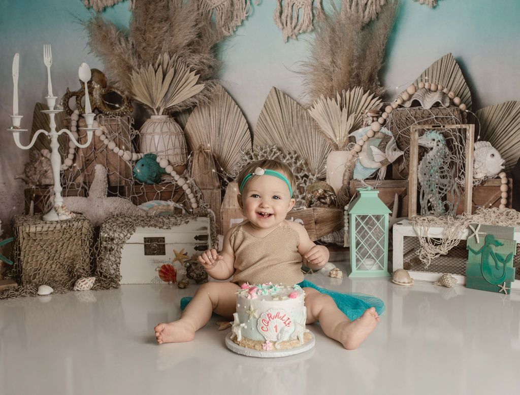 A baby is sitting on the floor with a cake in front of her.