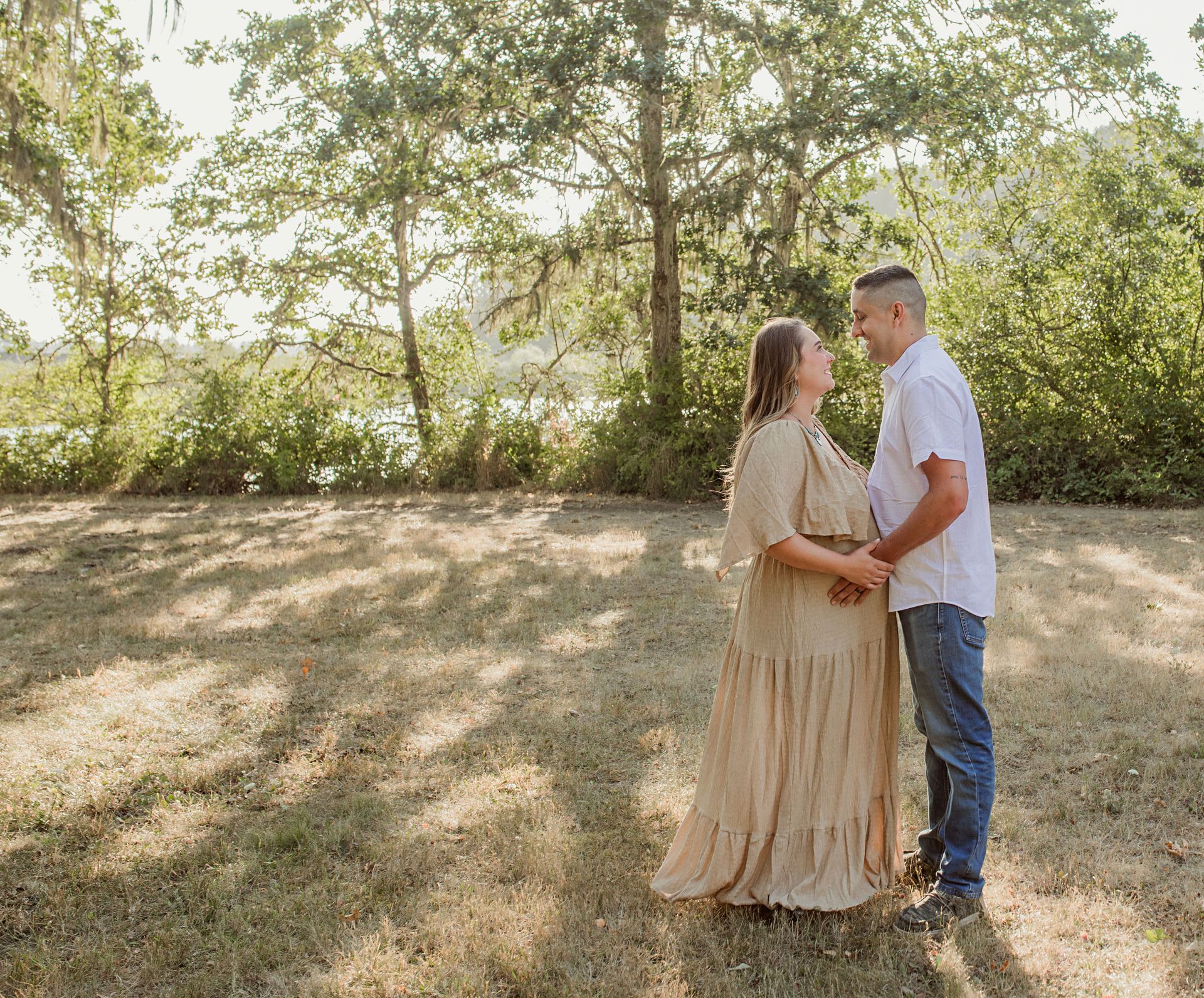 A man and a pregnant woman are standing in a field holding hands and kissing.
