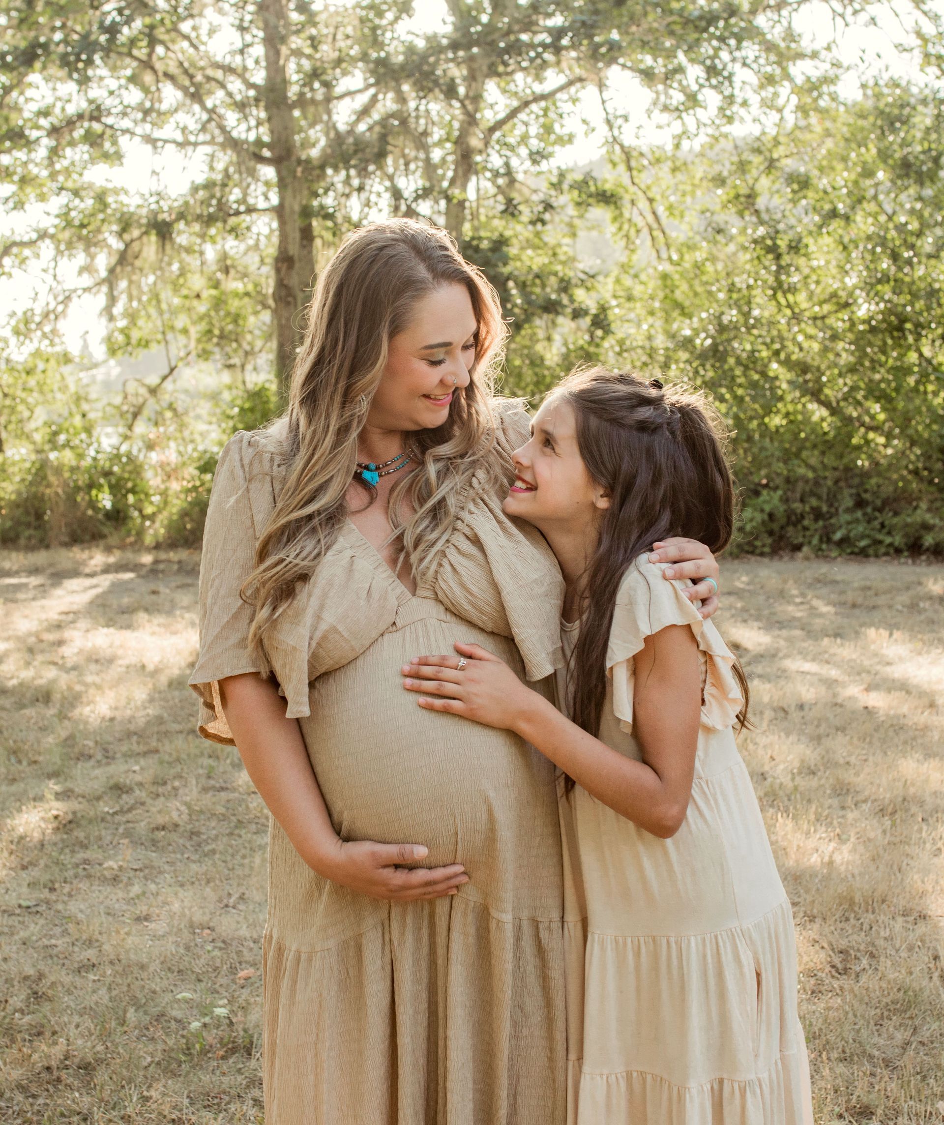 A pregnant woman and a little girl are hugging each other in a field.