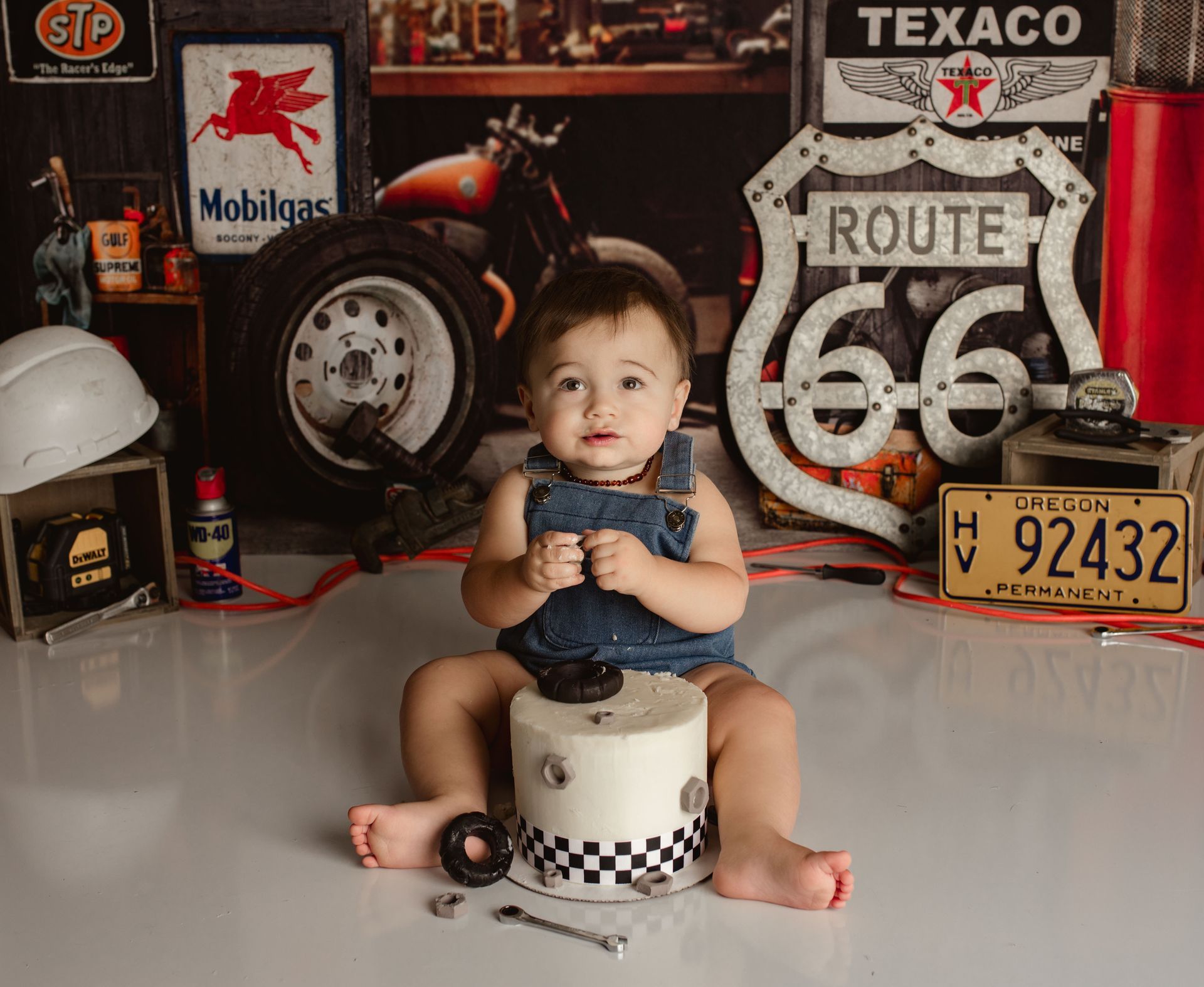 A baby is sitting on a cake in front of a route 66 sign. Cake Smash Photographer