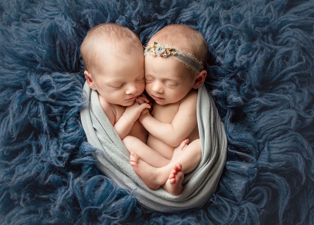 Two newborn babies are sleeping next to each other on a blue blanket. Twin baby photos