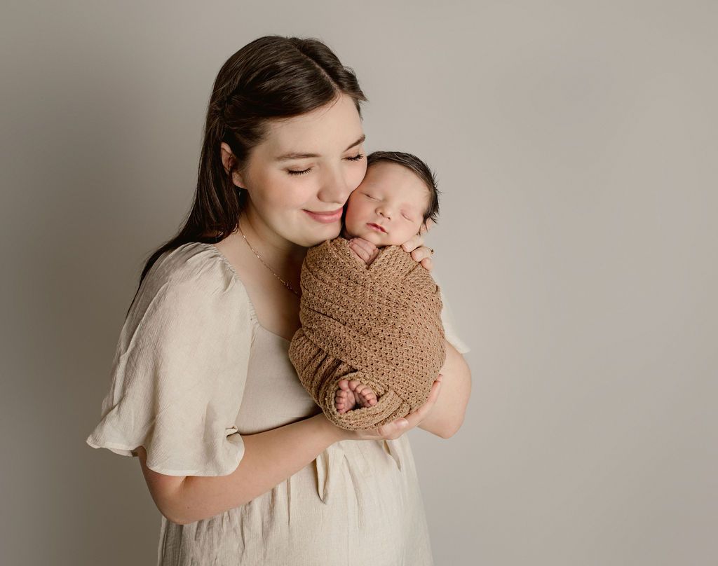 A woman is holding a newborn baby wrapped in a brown blanket. baby props