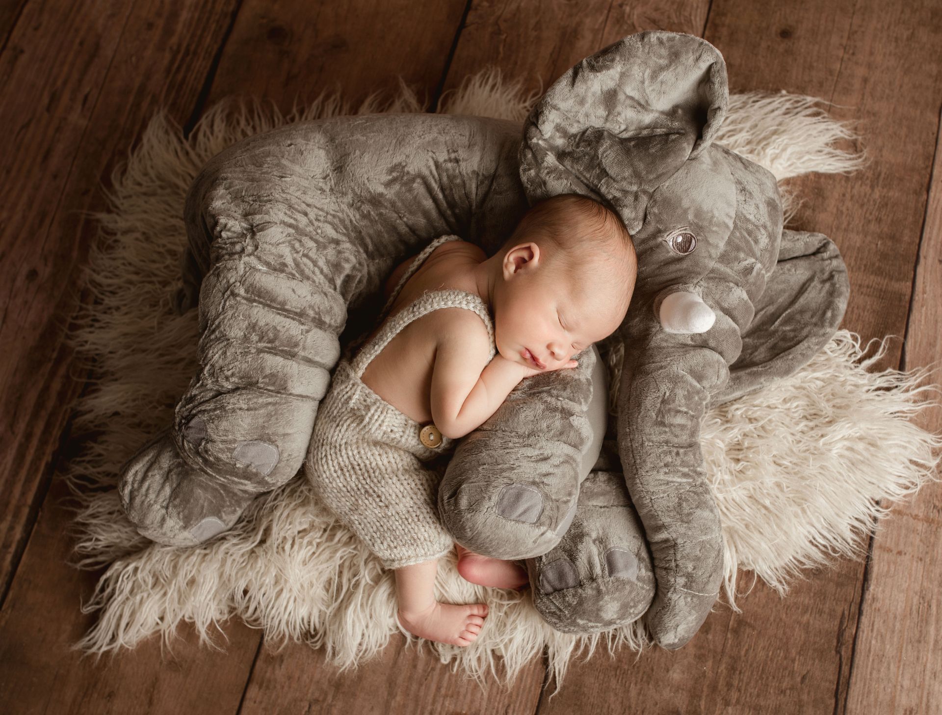 A newborn baby is sleeping next to a stuffed elephant.