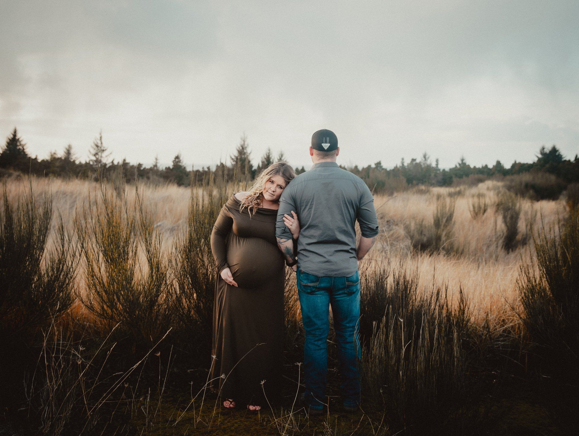 A man and a pregnant woman are standing in a field.