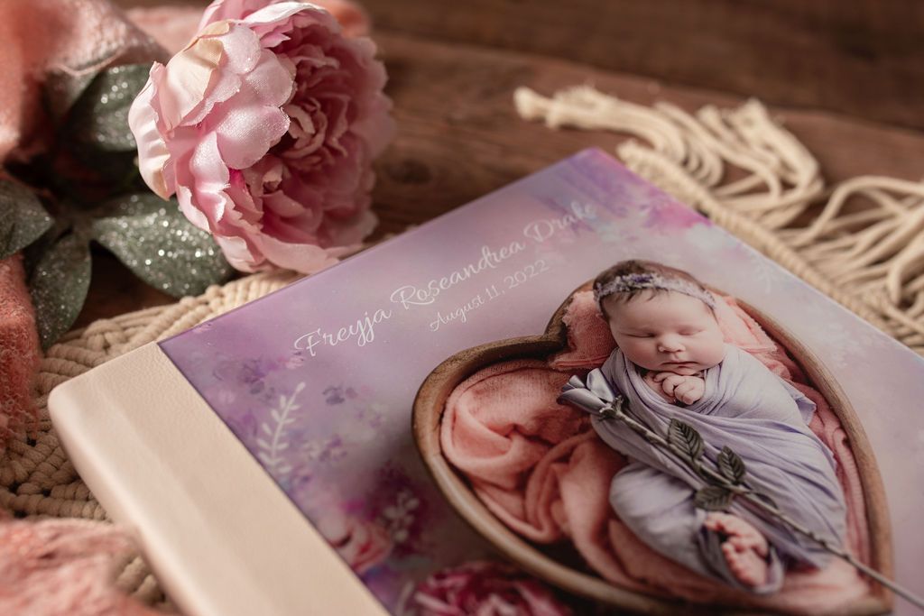 A book with a picture of a baby wrapped in a blanket is sitting on a table next to flowers.
