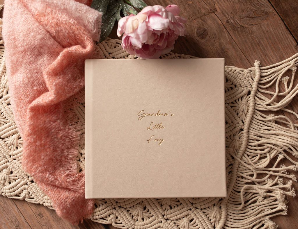 A book is sitting on top of a blanket on a wooden table next to a flower.