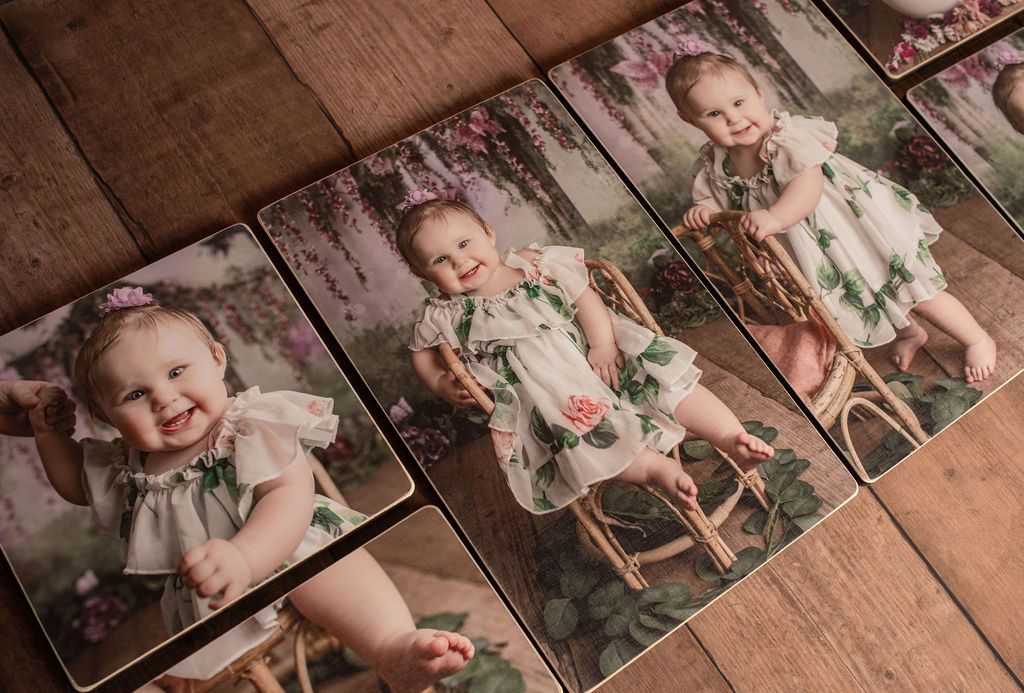 A baby in a floral dress is sitting in a rocking chair on a wooden floor.