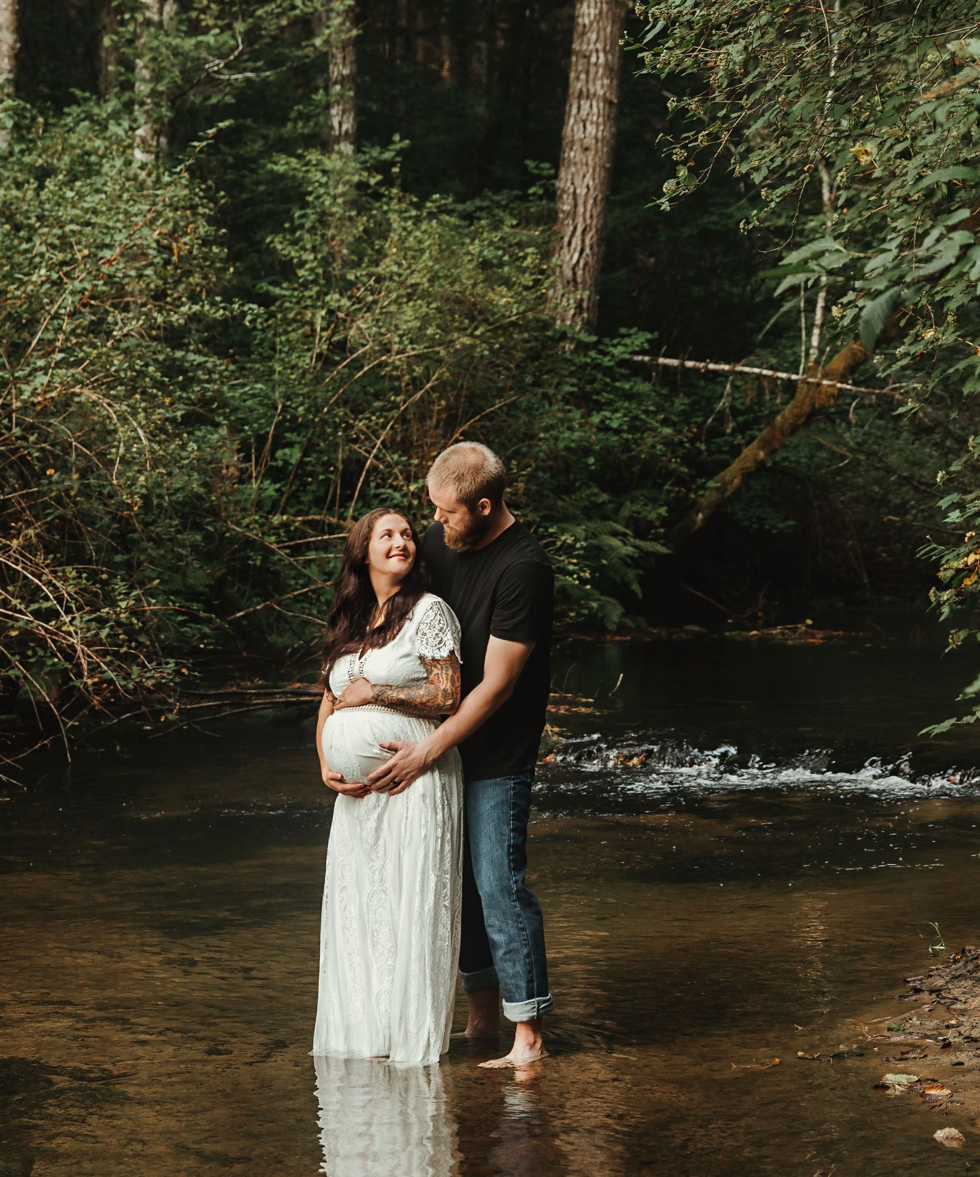 A man and a pregnant woman are standing in a river.