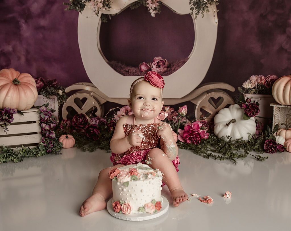 A baby girl is sitting on a table eating a cake.