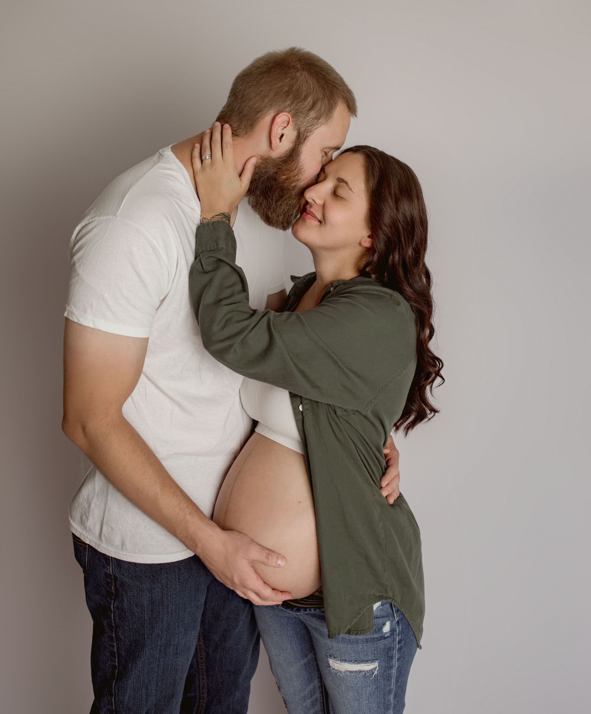 A man is kissing a pregnant woman on the cheek.