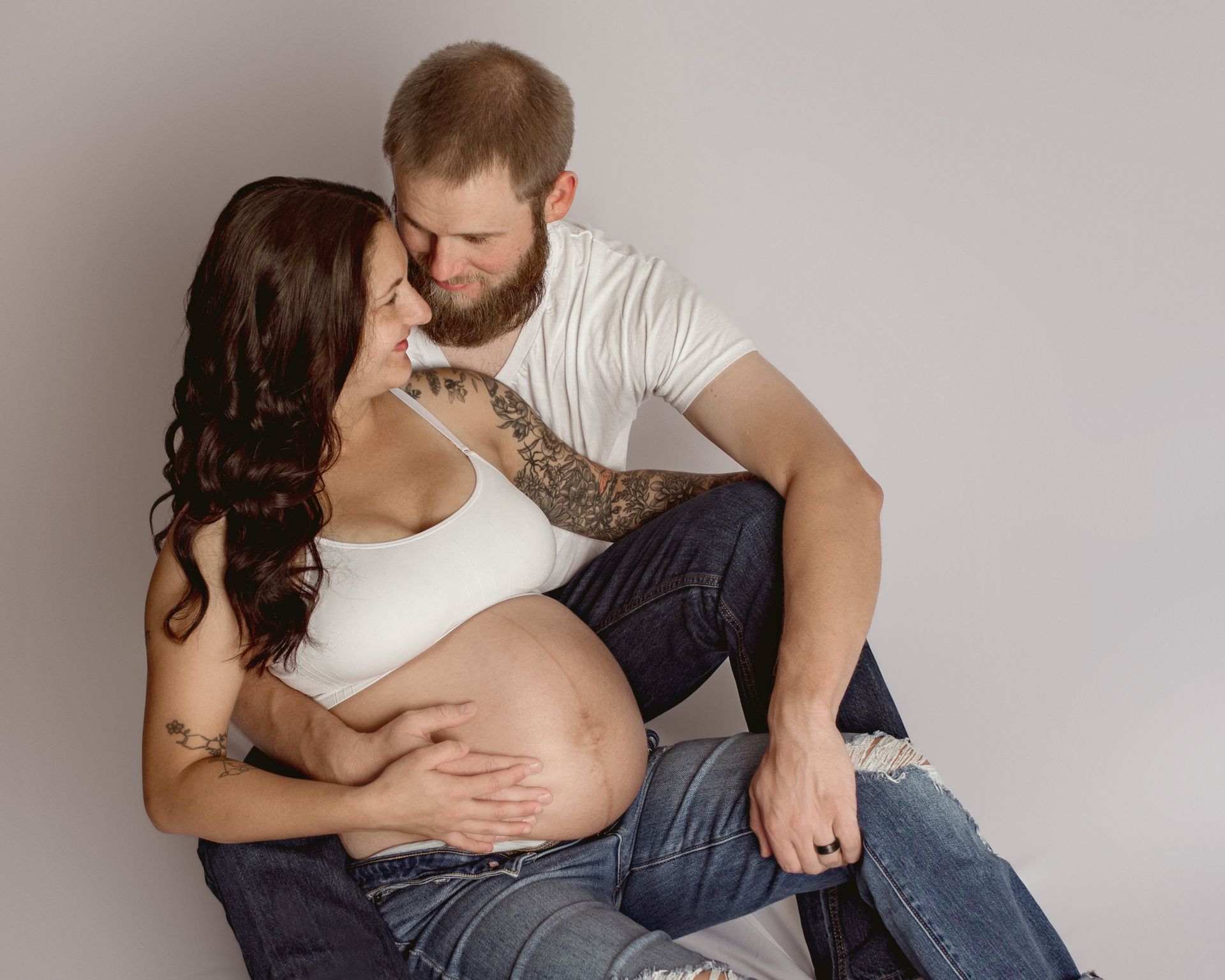 A pregnant woman is sitting on a man 's lap.