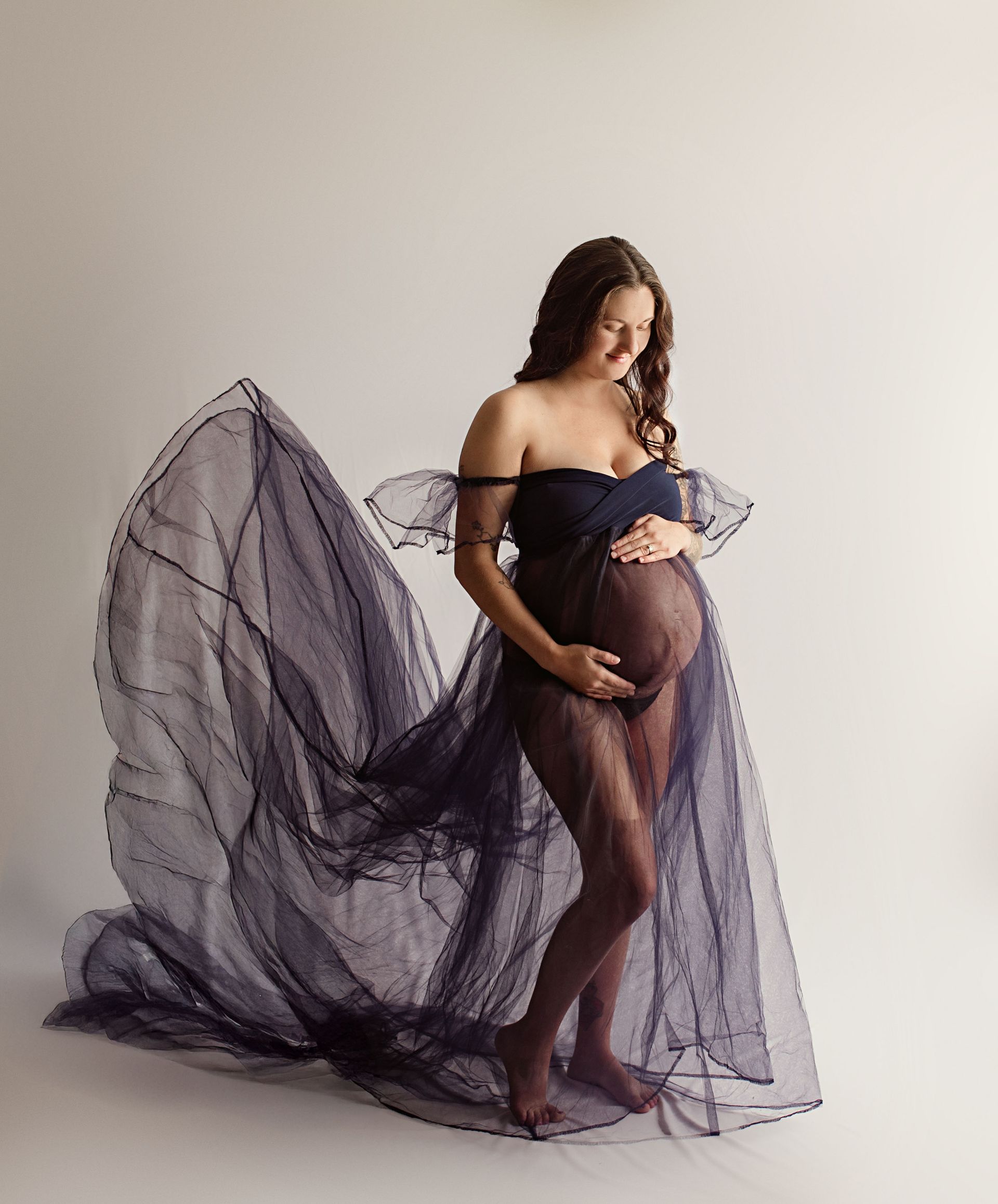 A pregnant woman is wearing a purple tulle dress and holding her belly.