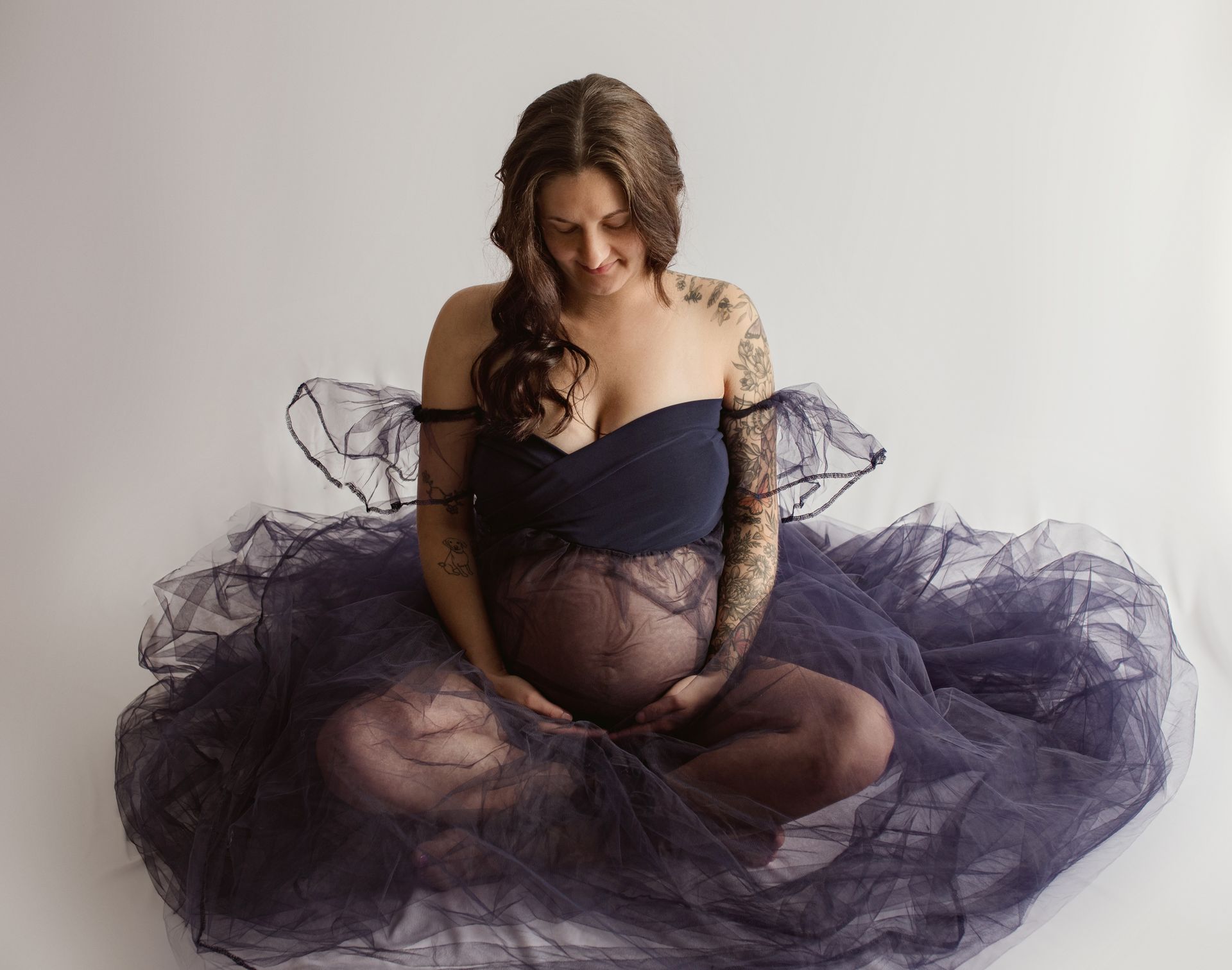 A pregnant woman is sitting on the floor in a purple dress.