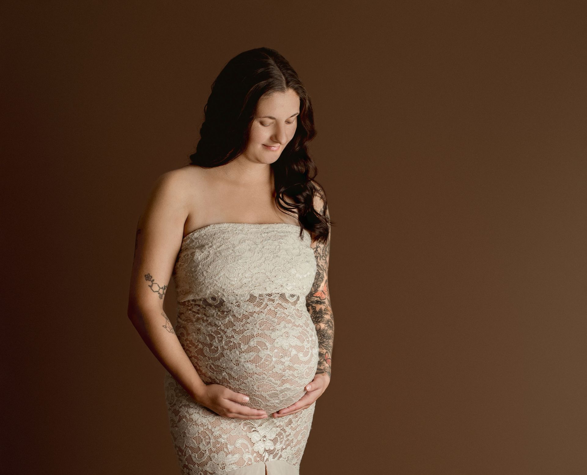 A pregnant woman in a white lace dress is holding her belly.