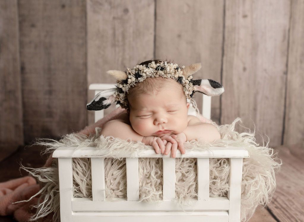 A newborn baby wearing a cow costume is sleeping in a white crib. newborn photographer near me