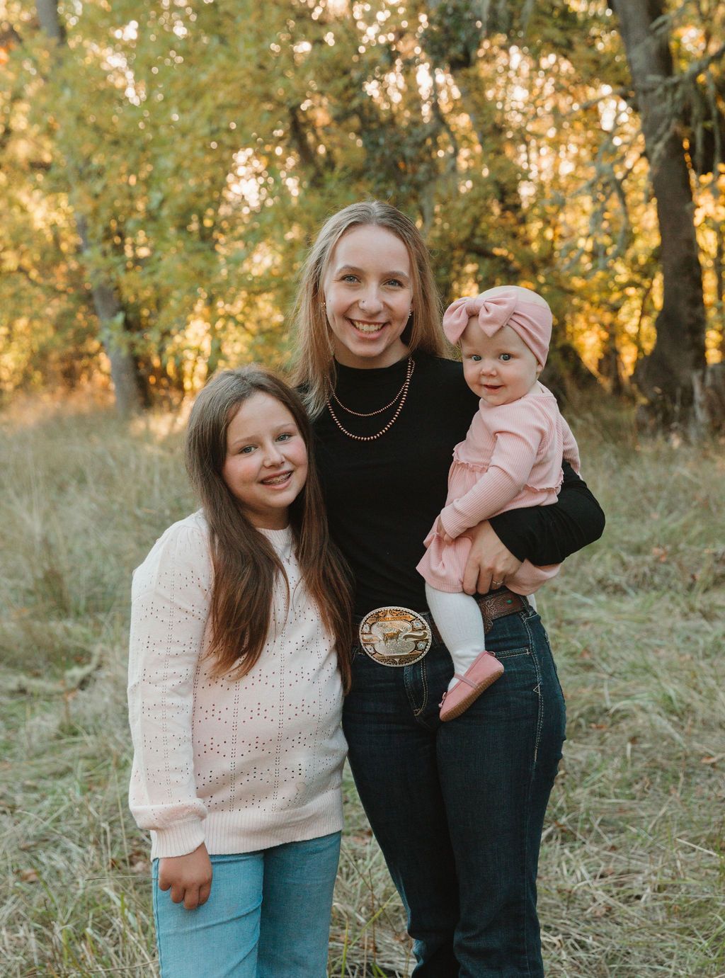A woman is holding a baby and two girls in a field.