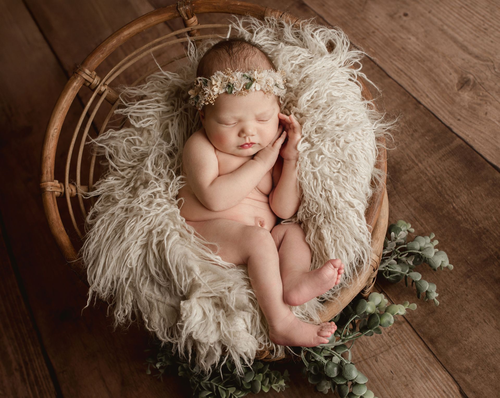 A newborn baby is sleeping in a wicker basket on a wooden floor.