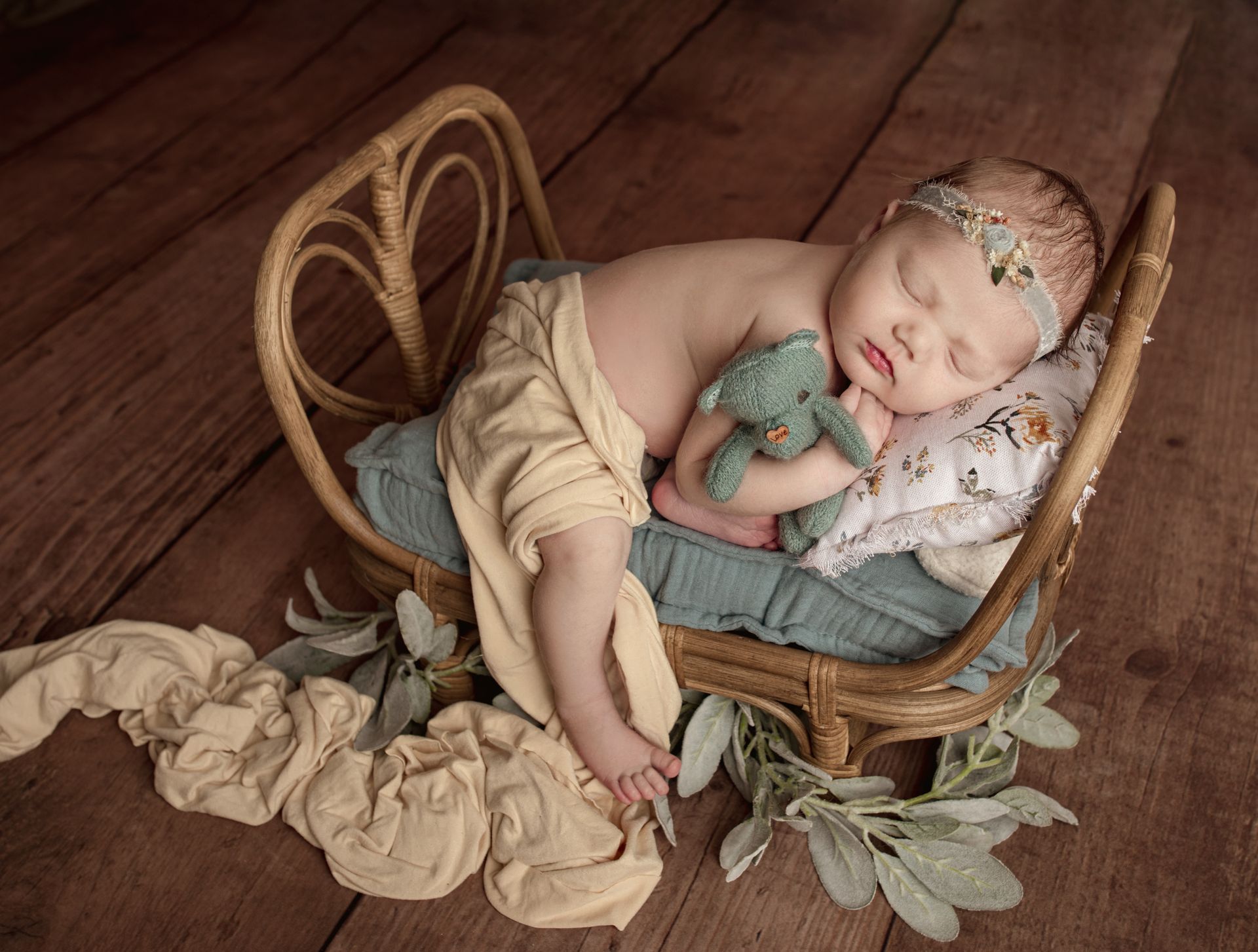 A newborn baby is sleeping in a wicker bed with a teddy bear.