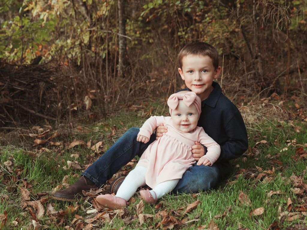 A boy and a baby girl are sitting in the grass.