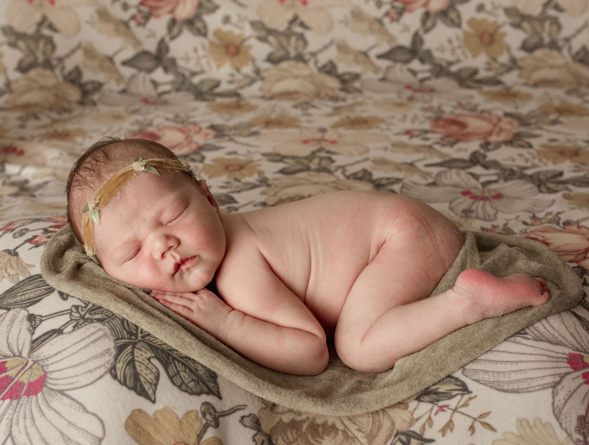 A newborn baby is sleeping on a floral blanket.