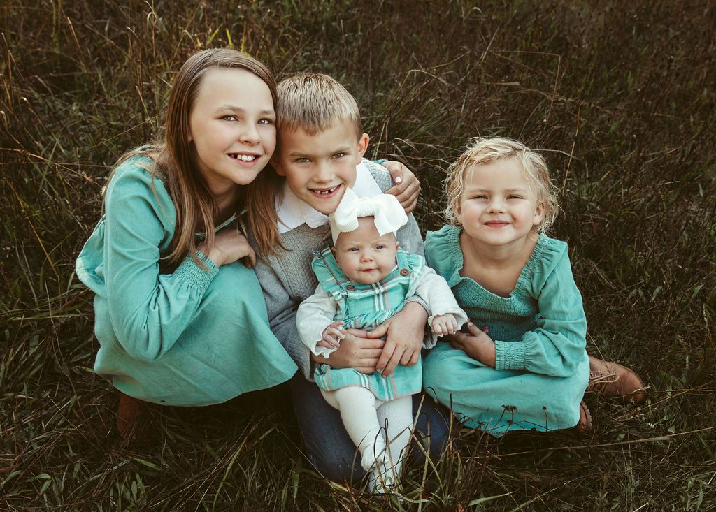 A group of children are posing for a picture while sitting in the grass.