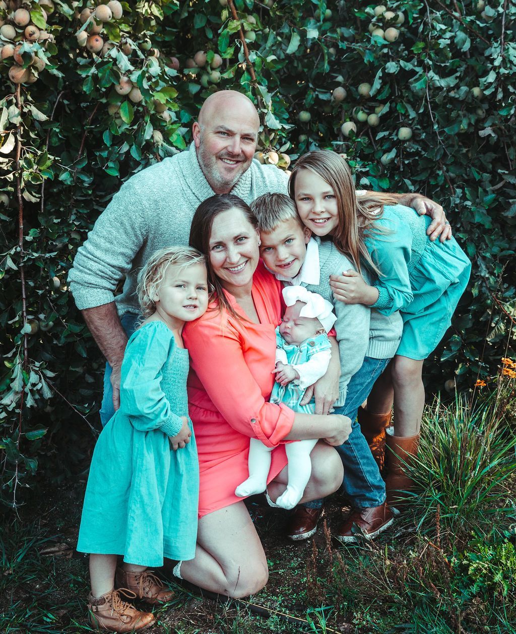 A family is posing for a picture in front of an apple tree.