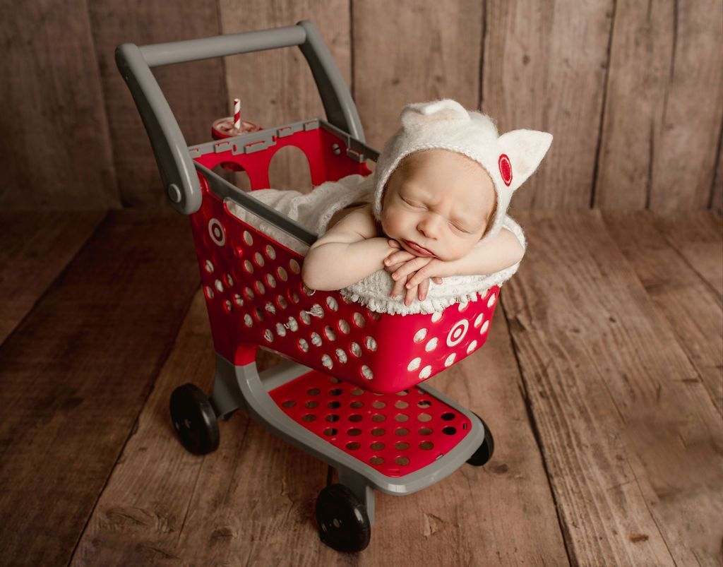 A newborn baby is sleeping in a shopping cart. Themed Baby Photos