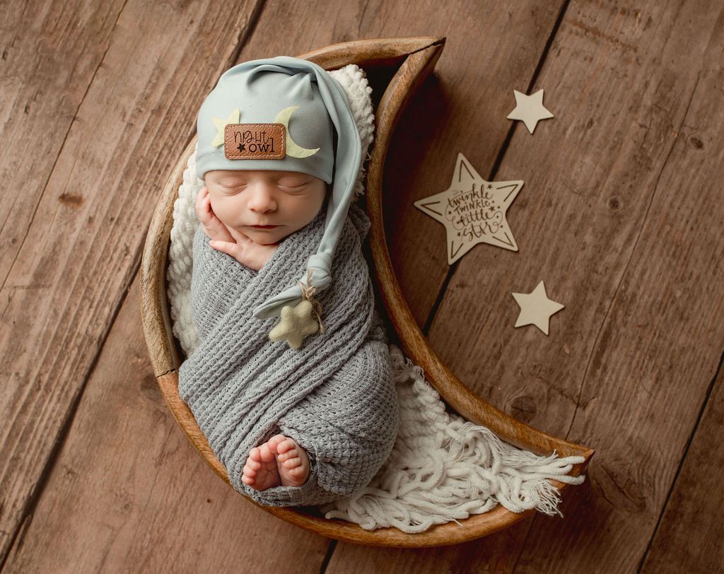 A newborn baby is wrapped in a blanket and sleeping on a crescent moon.
