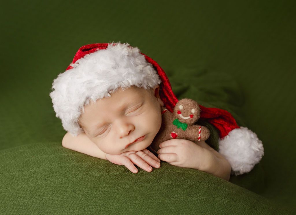 A newborn baby is wearing a santa hat and holding a gingerbread man.
