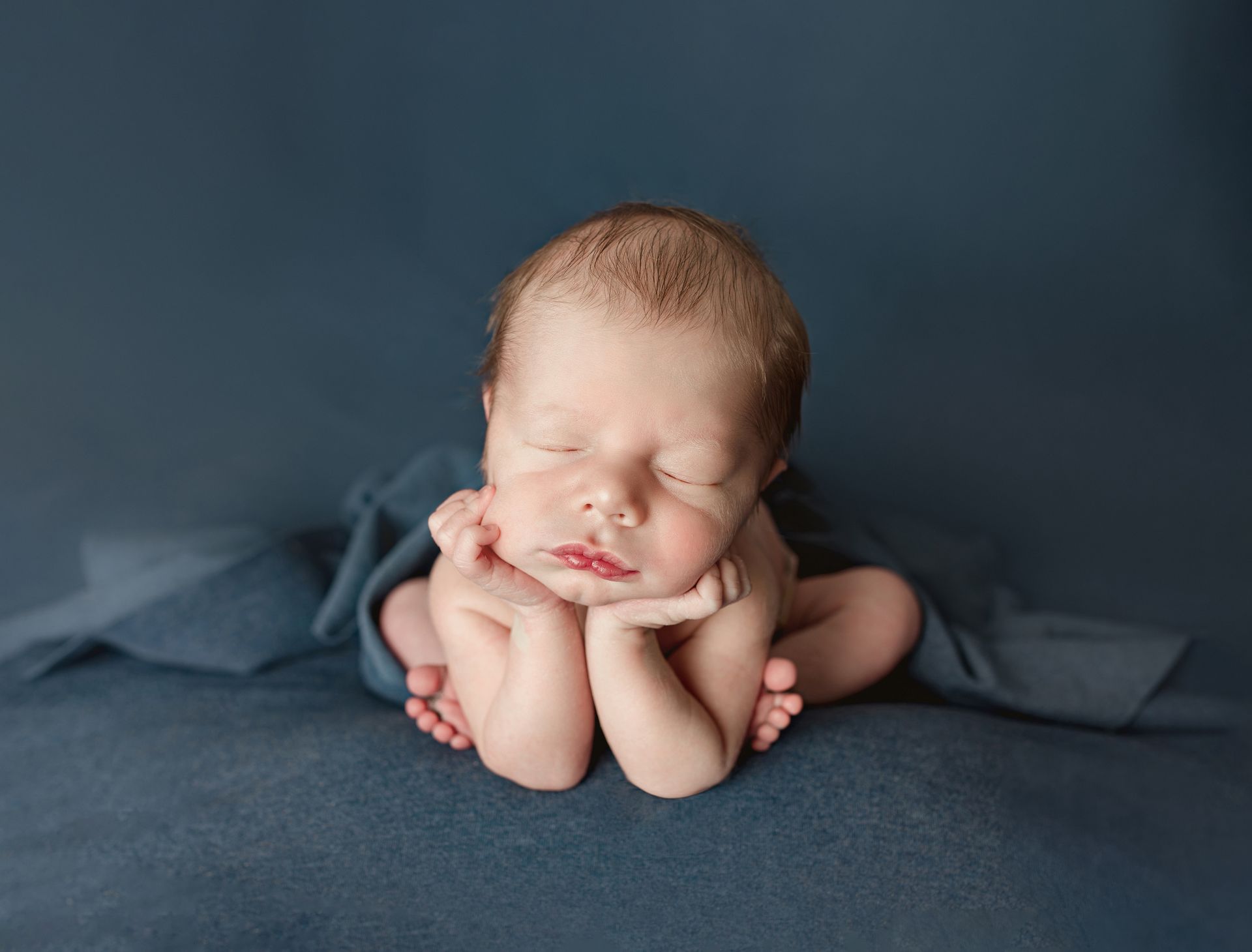 A newborn baby is sleeping on a blue blanket.