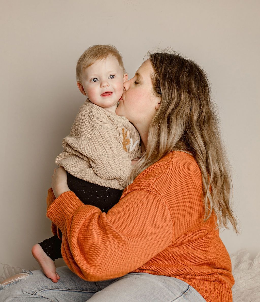 A woman is holding a baby in her arms and kissing it on the cheek.