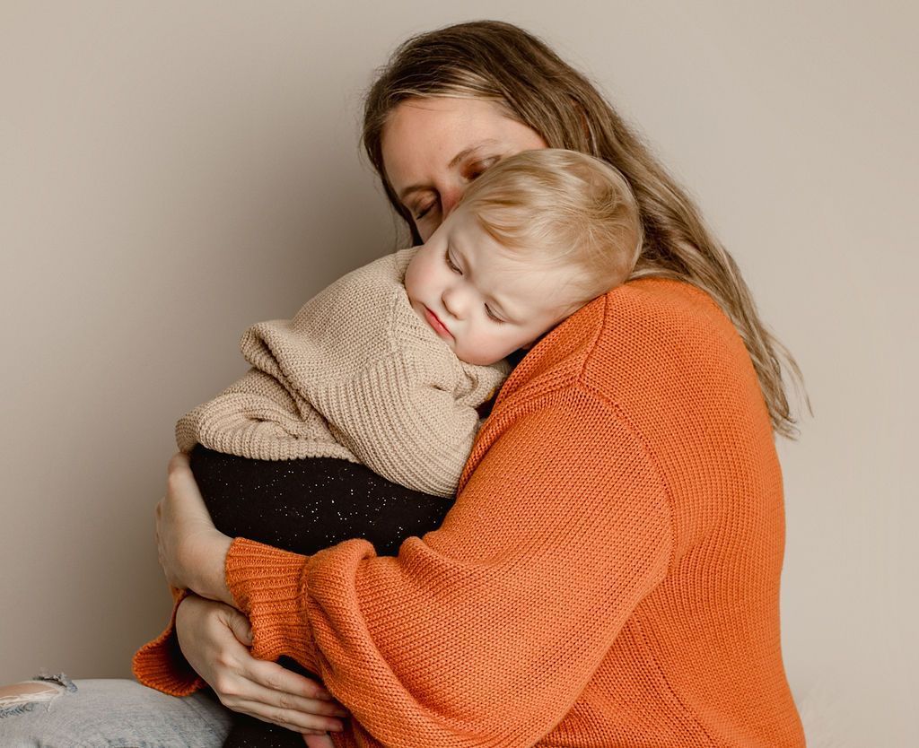 A woman in an orange sweater is holding a baby in her arms.