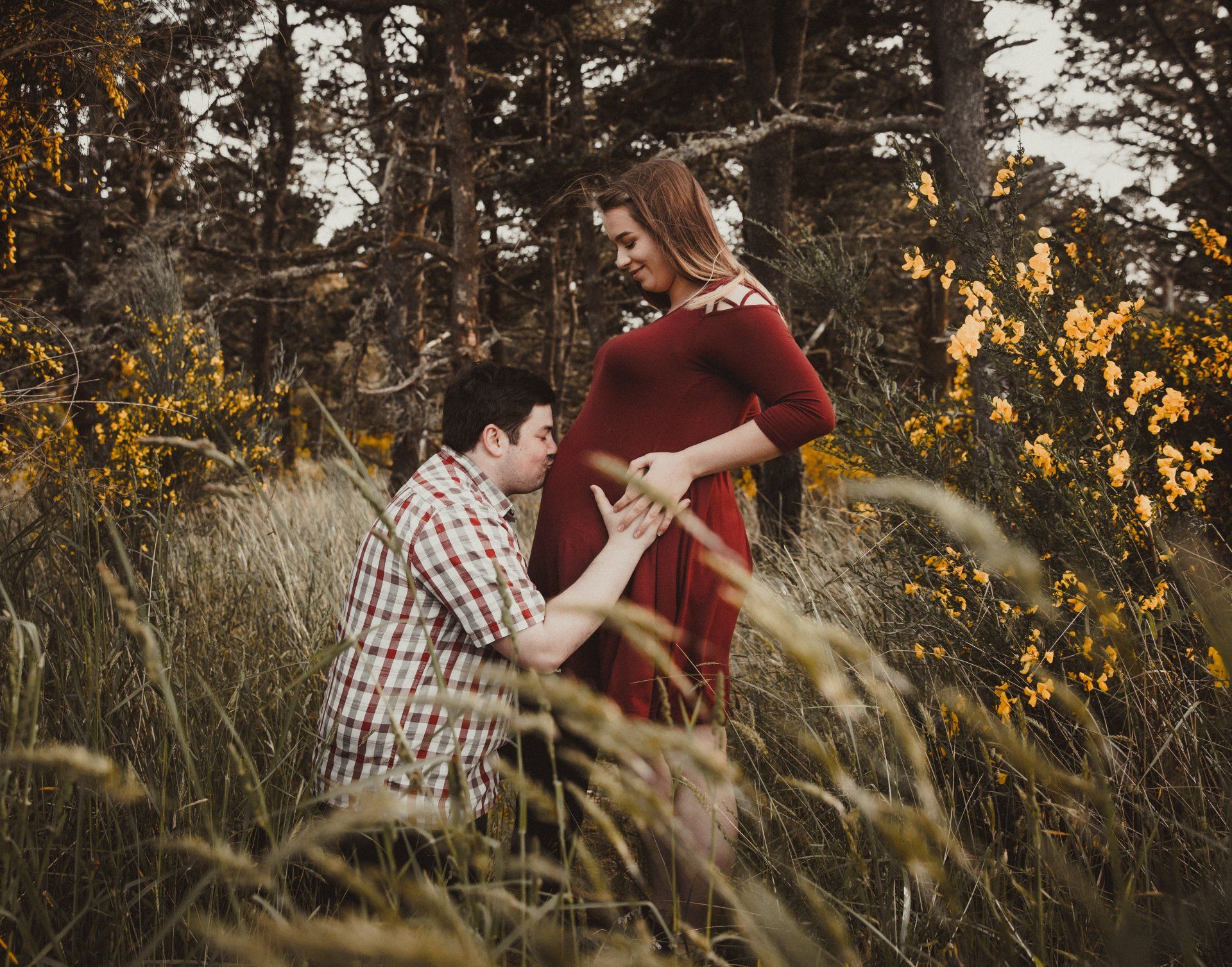 A man is kissing a pregnant woman 's belly in a field. Maternity photographer near me