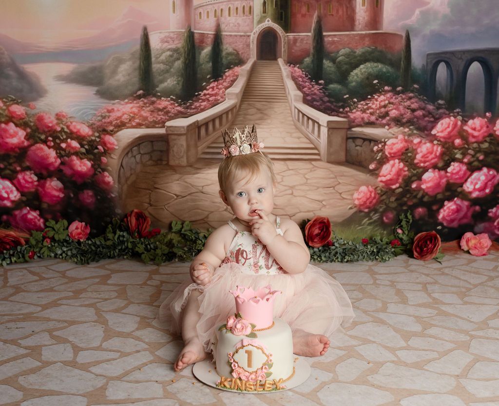 A baby girl is sitting on a cake in front of a castle.