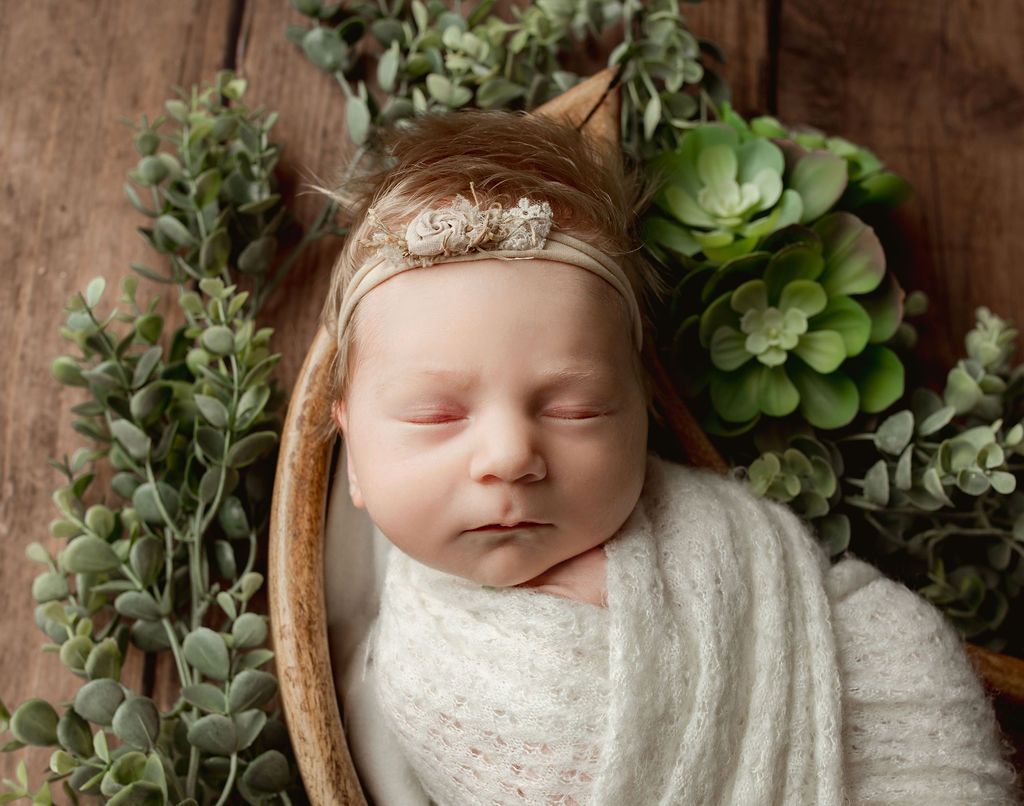 A newborn baby wrapped in a white blanket is sleeping on a wooden table.