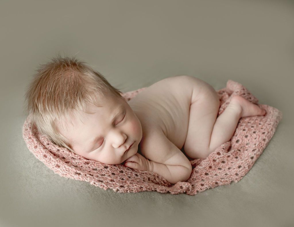 A newborn baby is sleeping on a pink blanket.