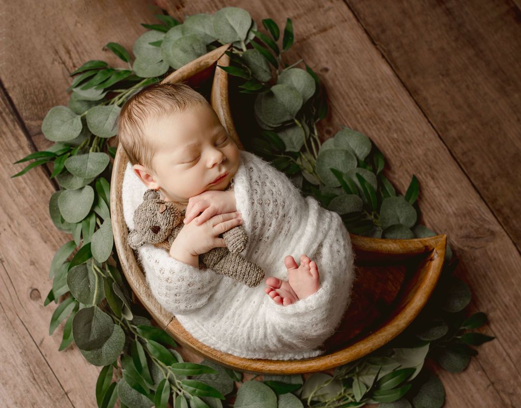 A newborn baby is sleeping in a basket with a teddy bear.